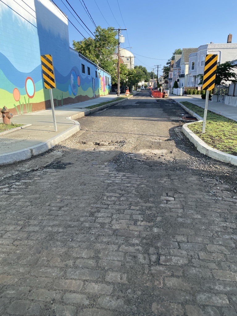Photo of a pinch point where the road narrows on Tufts Street, cobbles are seen along the roadway while a colorful mural is painted on the facade of a nearby building