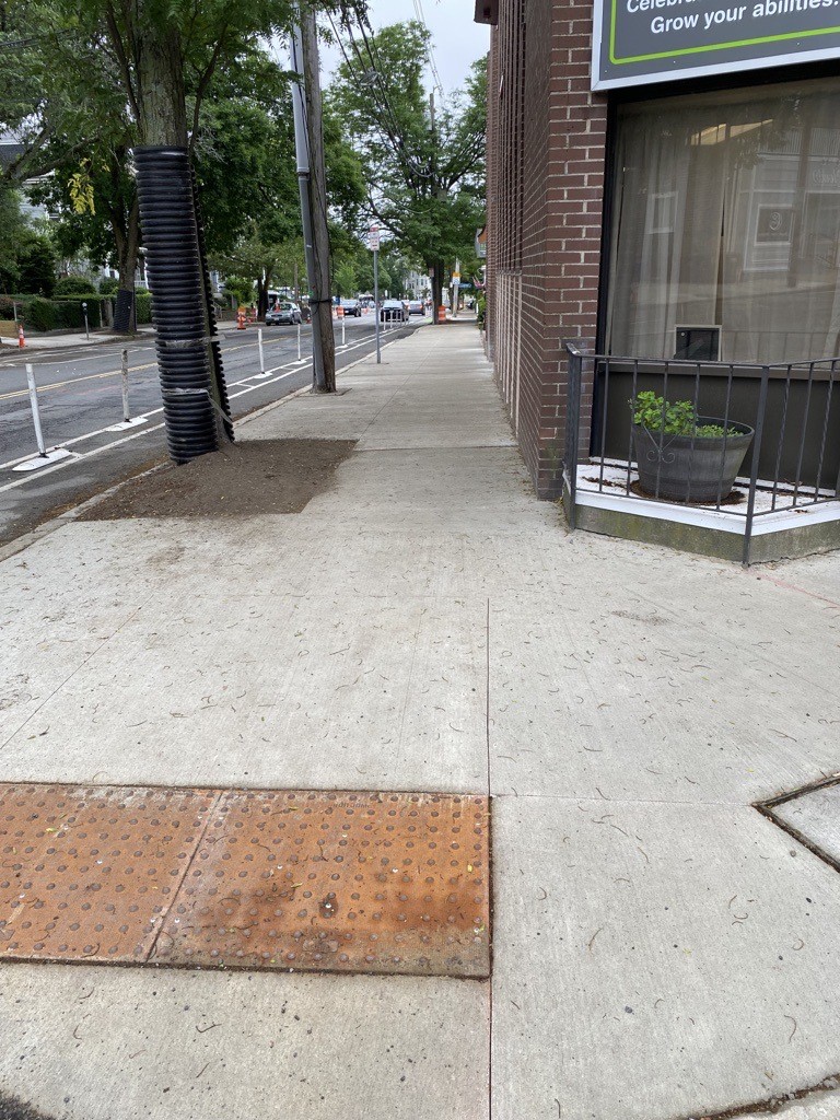 Newly constructed sidewalk on Holland Street with curb ramp and tactile warning pad in the foreground; facing west toward Davis Square on a cloudy day