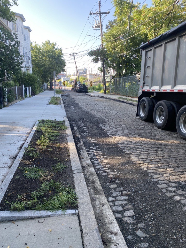 Photo looking down Tuft Street toward Washington St. The sidewalk is seen on the left and the roadway on the right with exposed cobbles in advance of pacing.