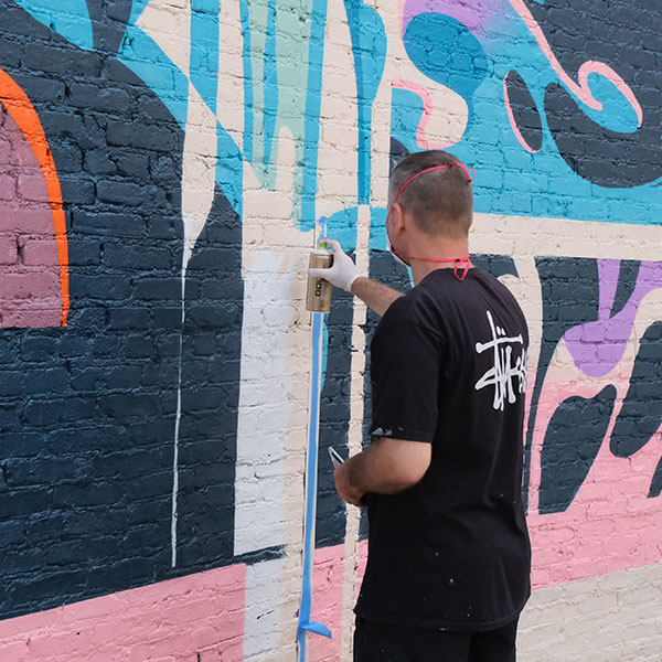 A person is painting a mural on a brick wall