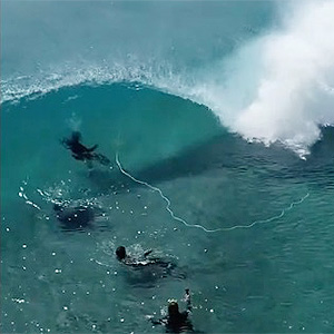 Researchers in wetsuits wait for wave to hit them.