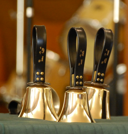 Three brass handbells sit on a green pillow. 