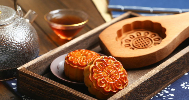 tray with wooden mooncake mold and 2 mooncakes with glass teapot and teacup behind them