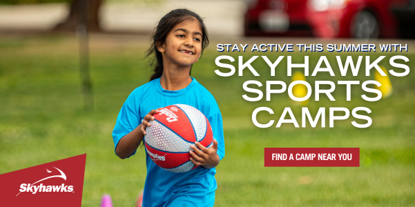 A young girl holds a basketball in a grassy park. The text reads. "Stay active this summer with Skyhawks Sports Camps. Find a camp near you." The Skyhawks logo is in the lower left.