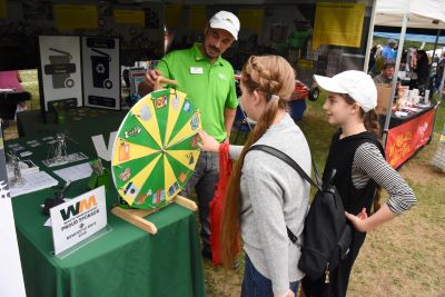 Two young people spin a yellow and green wheel at the WM booth at Newcastle Days