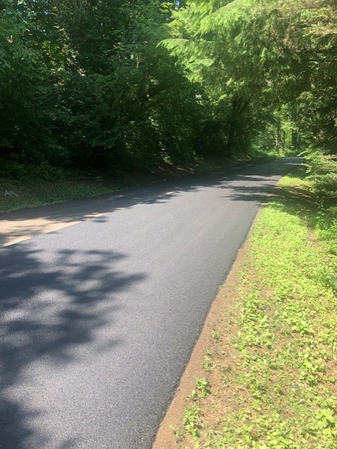A road with new, smooth pavement in a tree-lined area.