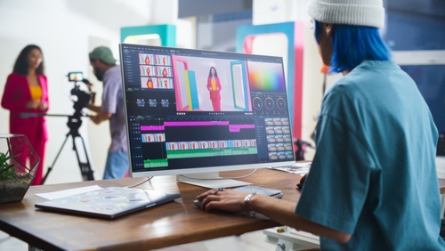 Young Caucasian Female Editor With Blue Hair Works On Video Editing Software_ While A Hispanic Male Videographer Records A Black Female Host In A Vibrant Studio Setting_ Enhancing Media Production.