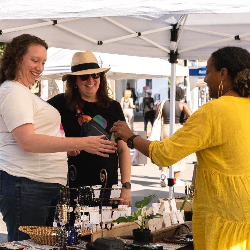 Two woman smiling across the table with a vendor who is giving a phone to one of them.. 