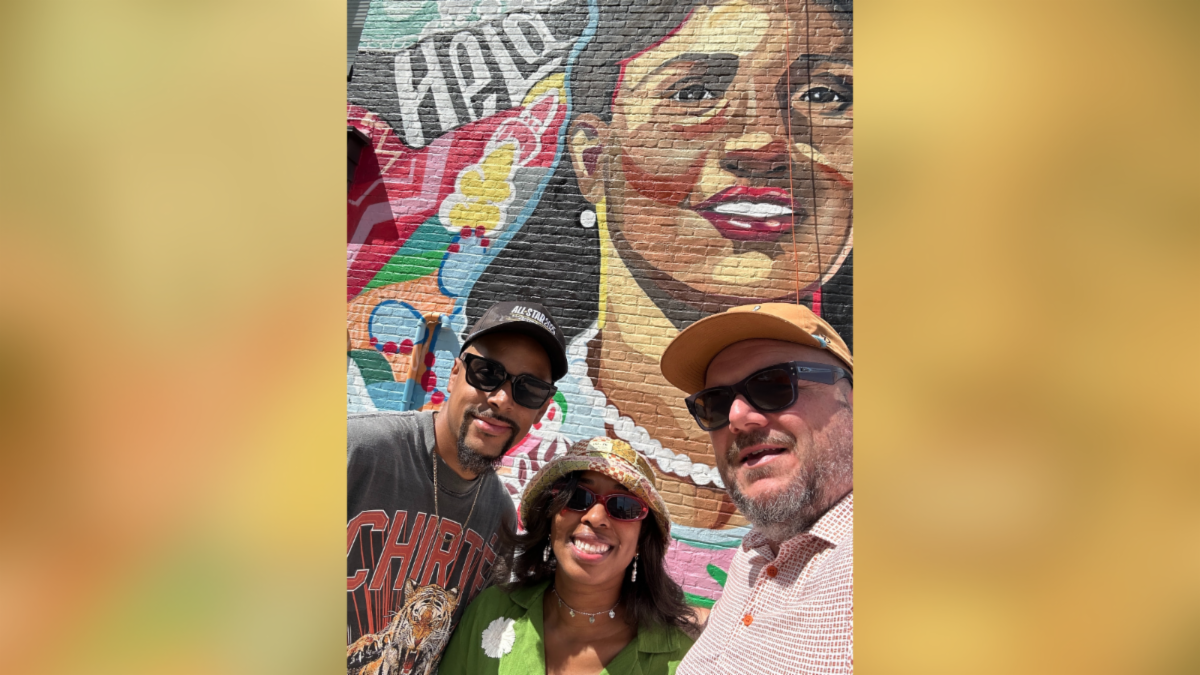 two men and one women smiling outside for selfie in front of Henrietta Lacks mural