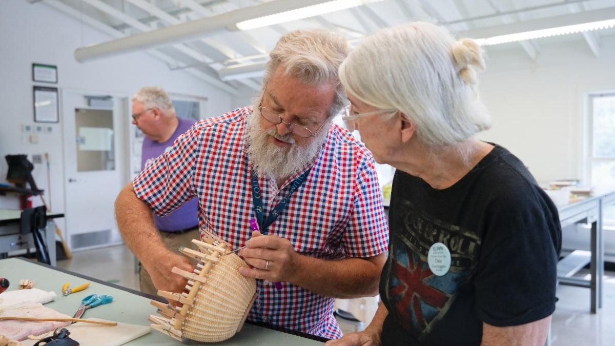 Older man and woman constructing a weaved basket by hand. 