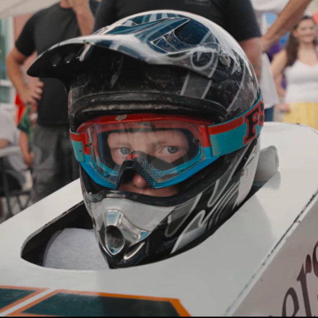 close up of child wearing racecar helmet in white derby car at standing point