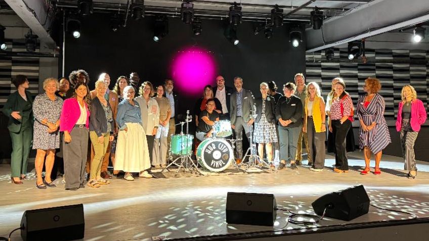 group of people on posed on stage with a person on the drums in the center