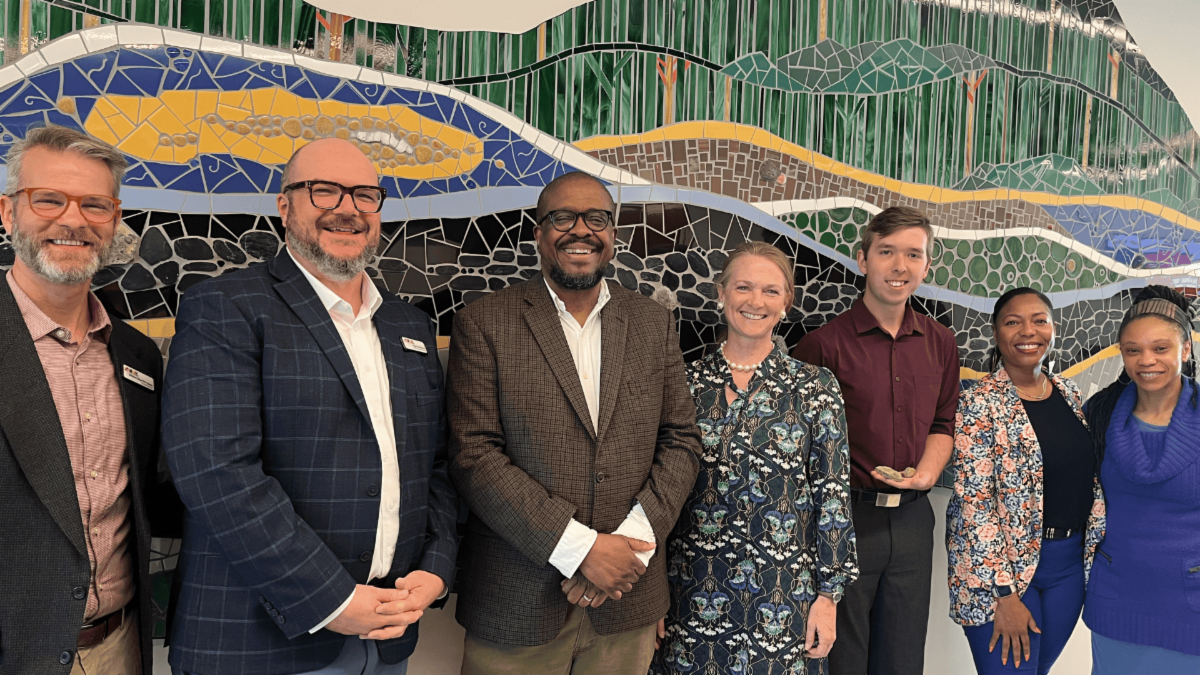 group of people smiling posed in front of mosaic public art installation by Stacia Goodman