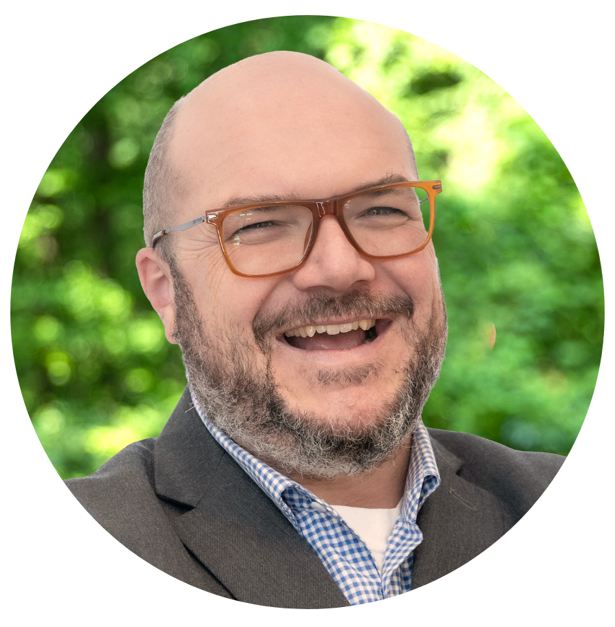 headshot of c. ryan patterson, public art program director for msac,smiling bald man with brownimmed glasses, beard and mustache, wearing dark gray blazer with light blue collared shirt.