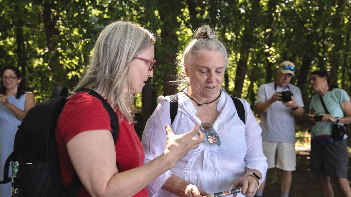 teaching artist in red shirt talking to student with smartphone in hand in front of other students and forest line