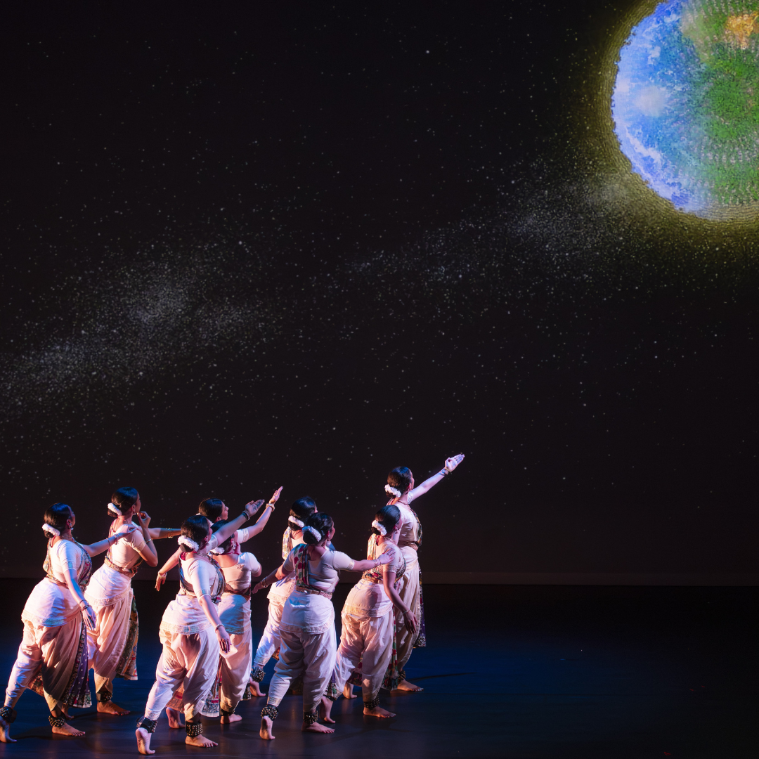 group of kuchi pudi dancers against black background looking up at blue and green sphere overhead