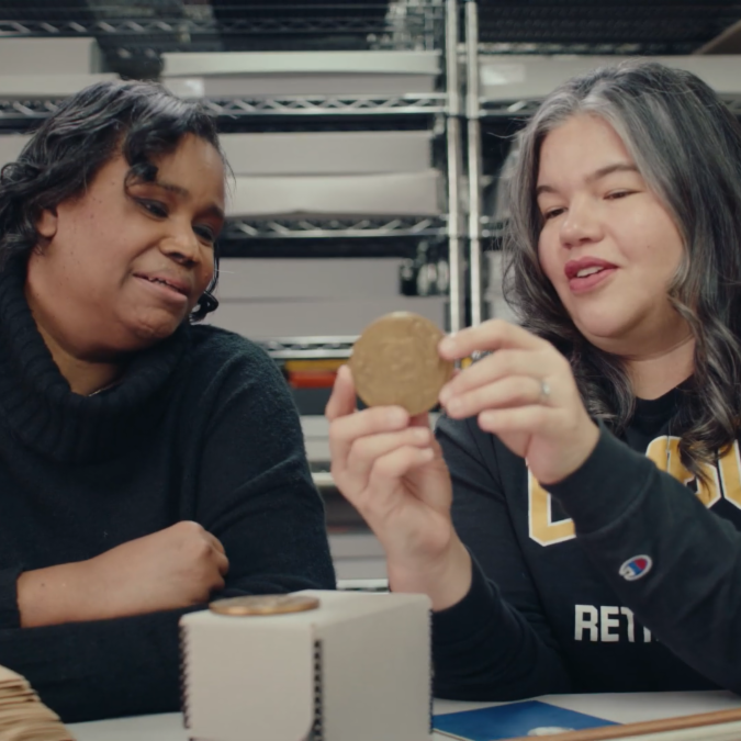 two woman looking at a medallion surrounded by archival shelves.
