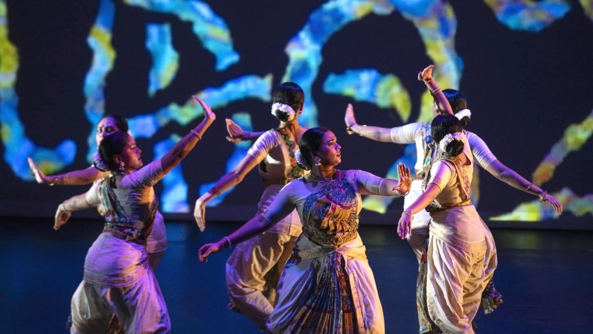 group of indian dancers performing on dark stage with blue and green circular visuals projecting on background