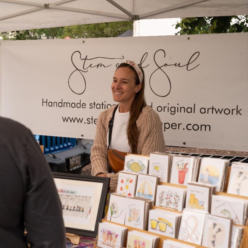 women vending art merchandise in front of business banner outside
