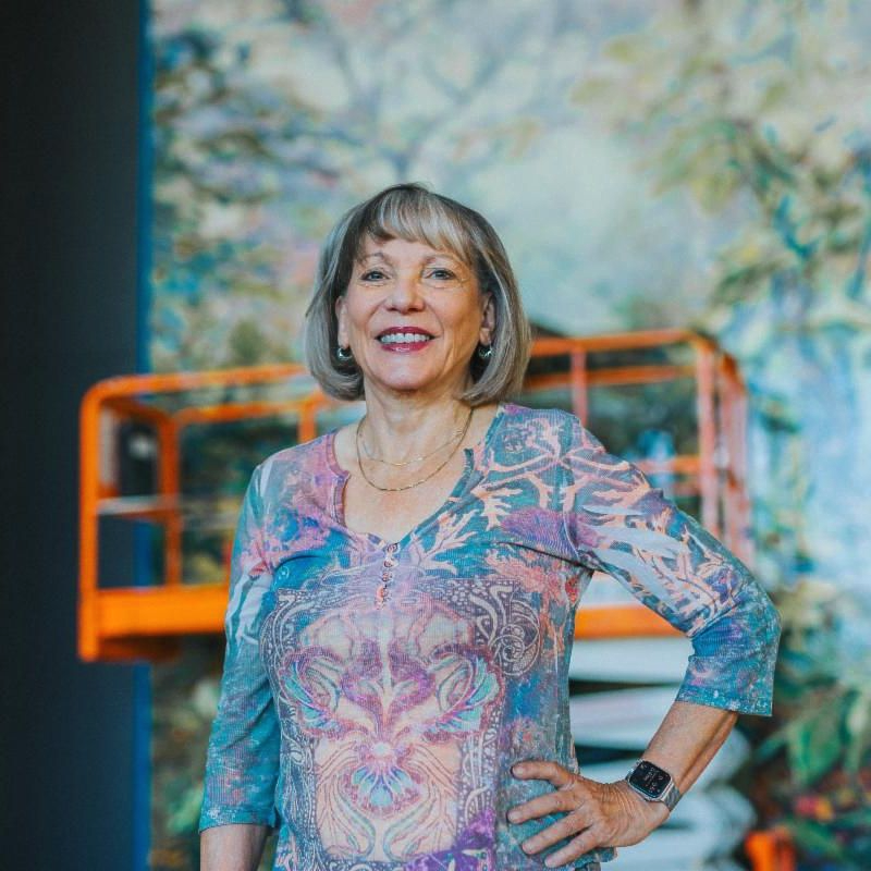 Public Artist Dixie Friend Gay posed smiling in front of a orange scaffold in front of her mosaic installation at Towson University.