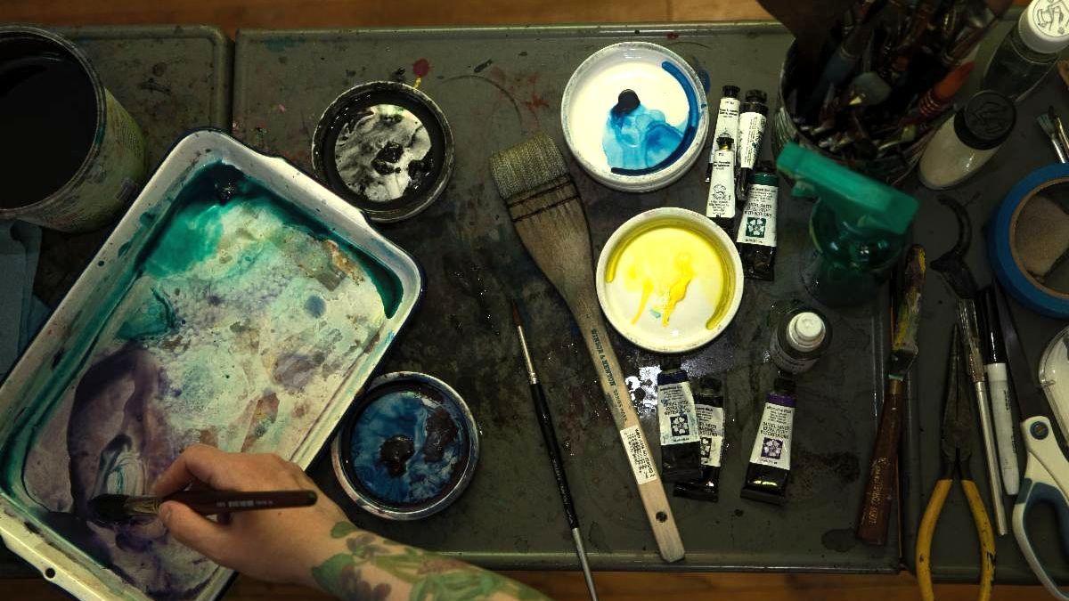 hand holding paint brush surrounded by painting supplies