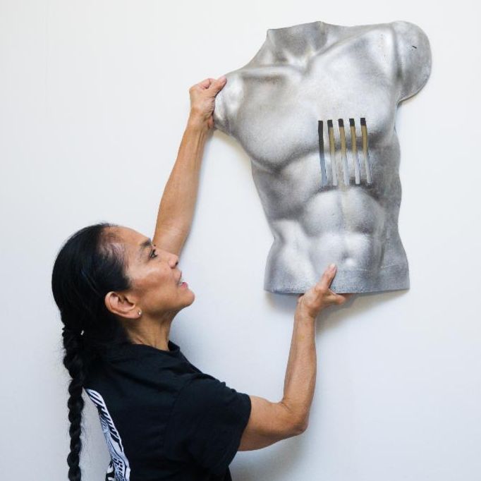 woman in black graphic tee placing a sculpture of a man's torso on a white wall. 