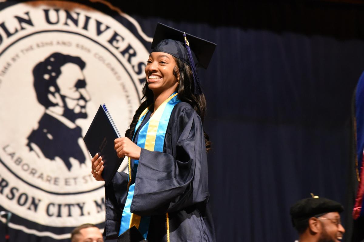 Photo of a Lincoln University of Missouri student walking across the stage at graduation with her diploma in hand.
