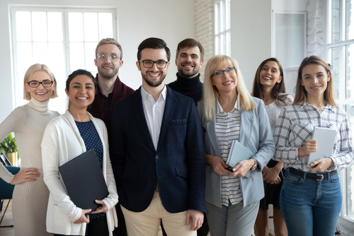 Group portrait of happy diverse colleagues of different ages. United businesspeople of 30s and 50s looking at camera. Team of trainee interns and coaches posing together in office. Teamwork concept