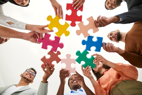 Diverse multiracial multi ethnic team of happy smiling adult men and women holding colorful jigsaw puzzle parts_ bottom view_ from below. Modern business_ teamwork_ education_ innovative ideas