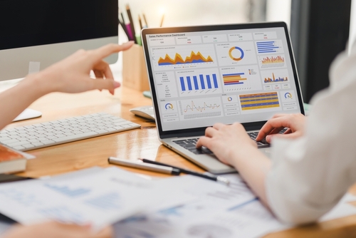 Two businesspeople or an accountant team are analyzing data charts_ graphs_ and a dashboard on a laptop screen in order to prepare a statistical report and discuss financial data in an office