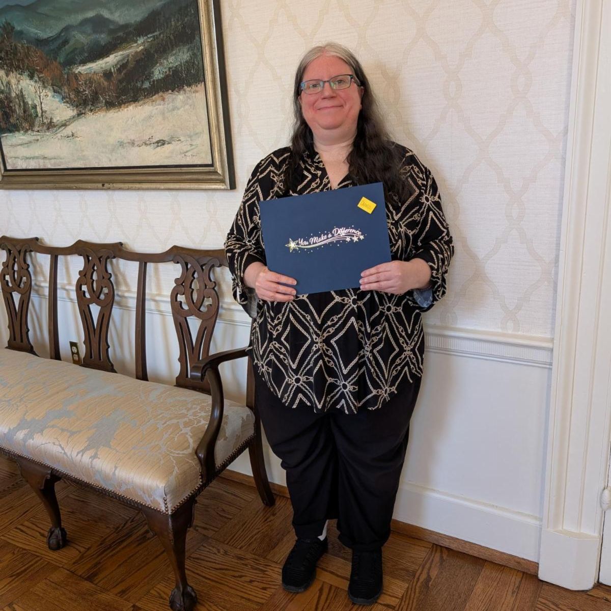 Person standing next to a bench holding a blue certificate.