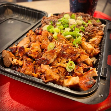 Tray of grilled chicken and beef topped with green onions and sesame seeds, served with a drink on a red cafeteria tray