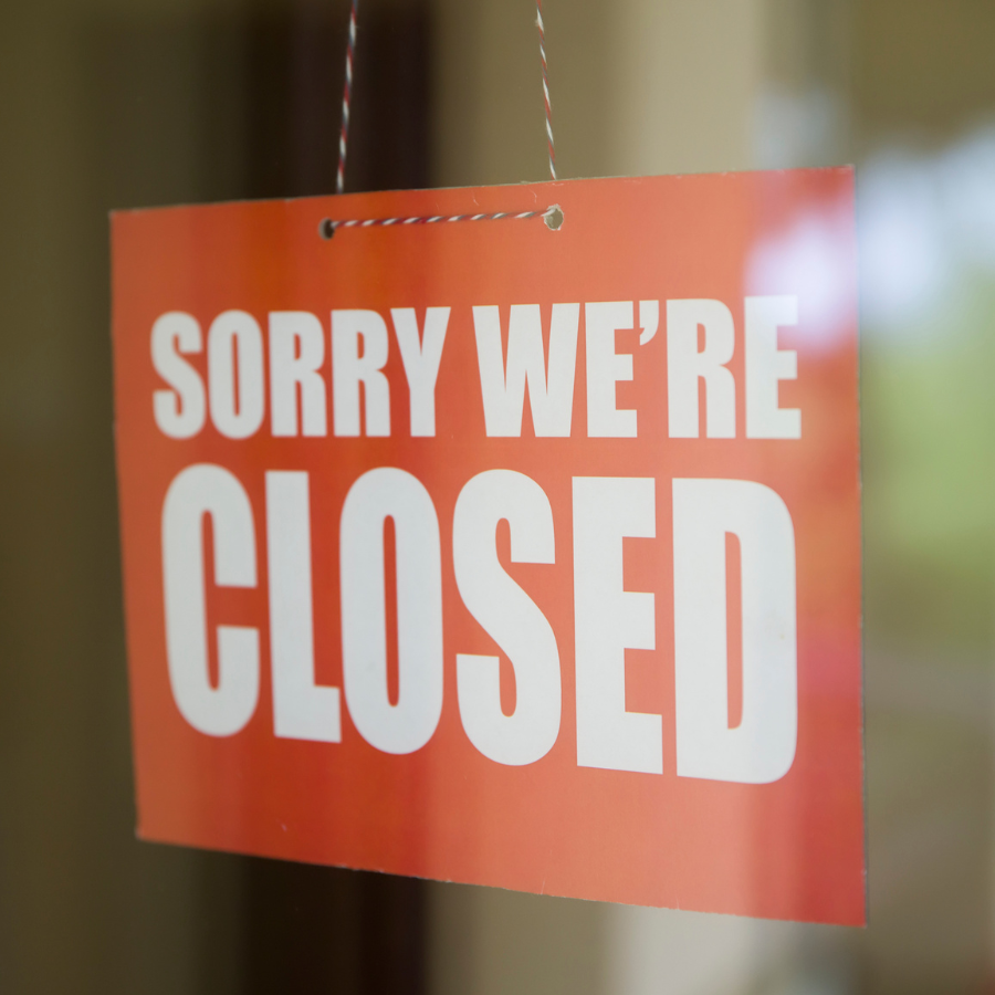red closed sign with white text saying sorry we're closed behind a window