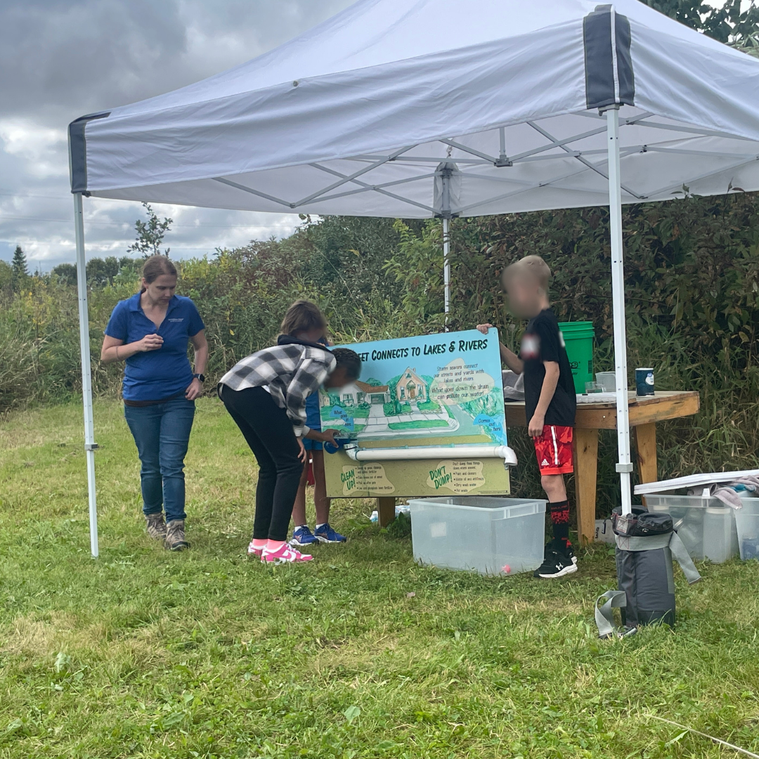 Students pour pretend stormwater pollutants down a storm drain, emptying into the Vermillion River (a plastic bin) at the Water Station..