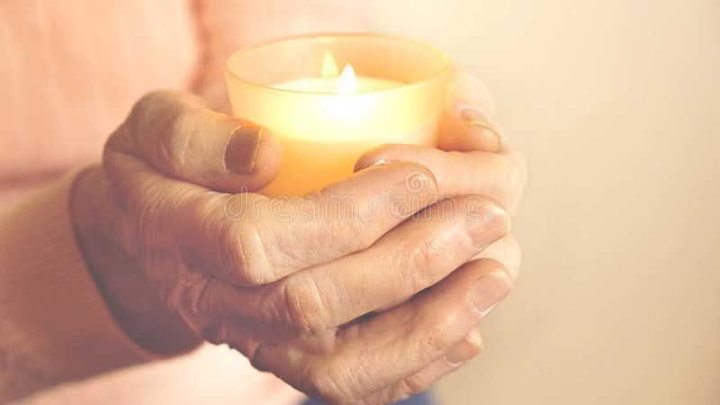 Hands hold a lit candle.