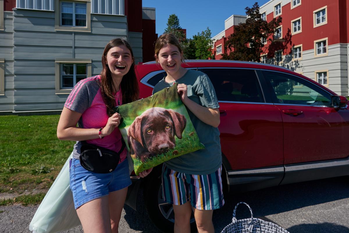 Students on move-in day smile and hold up a pillow with an image of a dog