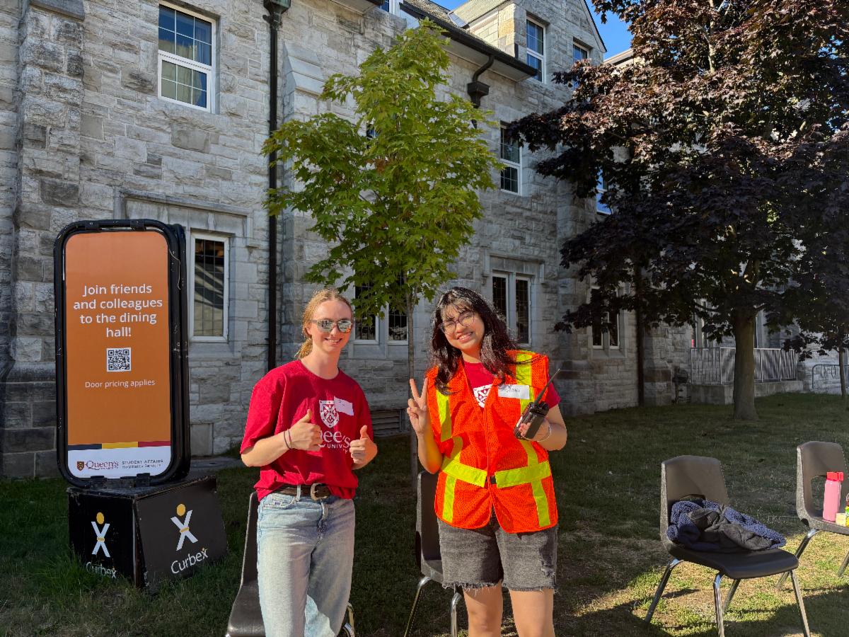 Two move-in day volunteers pose with their thumbs up by Ban Righ dining hall