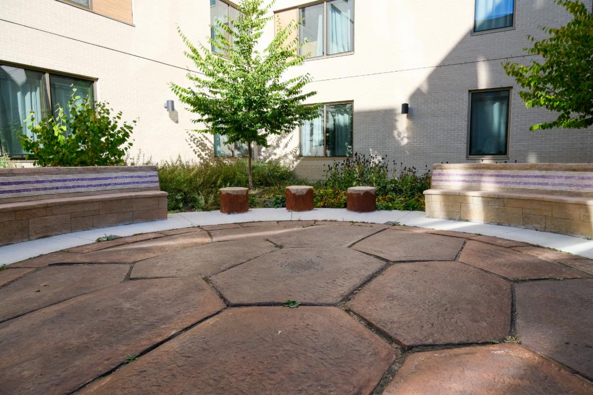 Endaayaan – Tkanónsote courtyard featuring stools, benches with the Two-Row Wampum, and a stne centre representing the shell of a turtle.