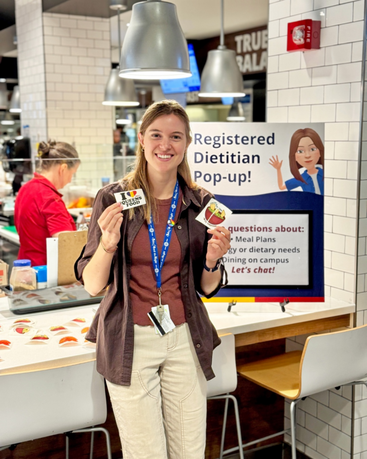 Amy Sebo, Registered Dietitian, smiles, holding stickers in the dining hall.