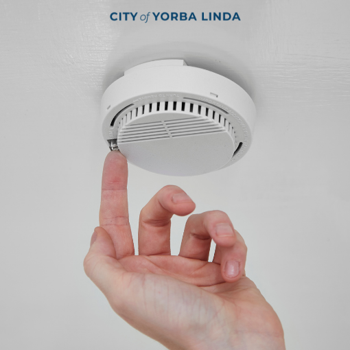 A finger pressing the "test alarm" button on a smoke alarm.