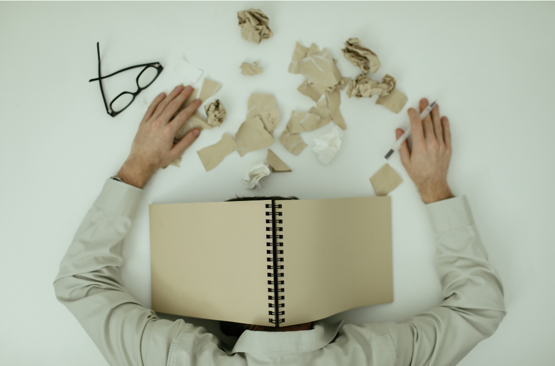 Person with head covered by book surrounded by crumpled paper