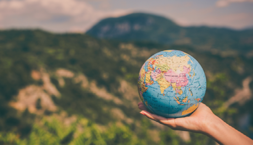 Hand holding globe in front of mountains
