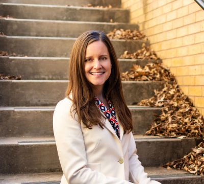 Portrait of Angela Calcaterra smiling in a blazer in front of a staircase