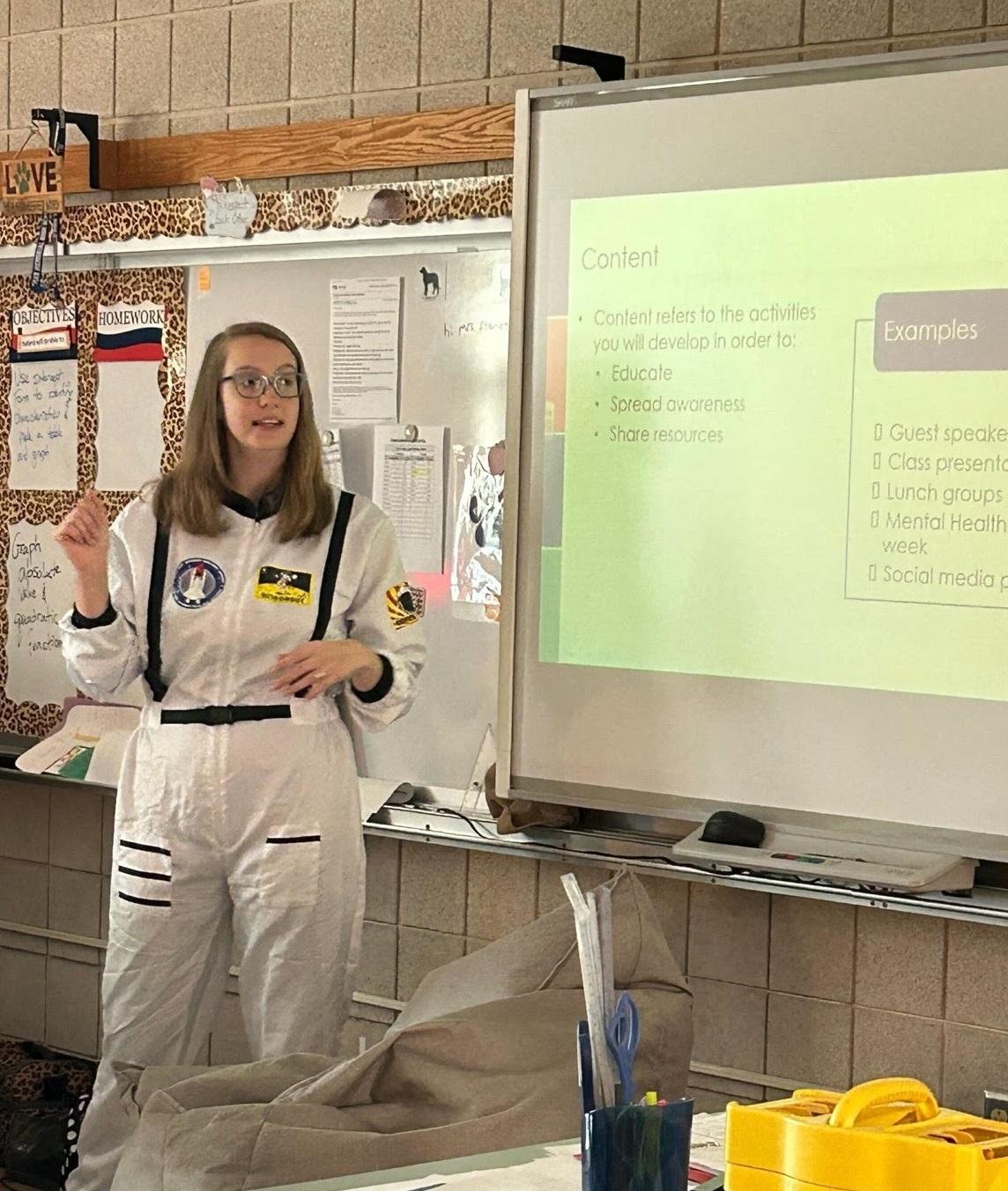 Mackenzie Wink presenting a mental health training in a school classroom. It was Halloween, so she is wearing an astronaut costume!