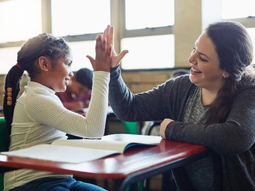 Teacher and elementary age child high-five over a desk.