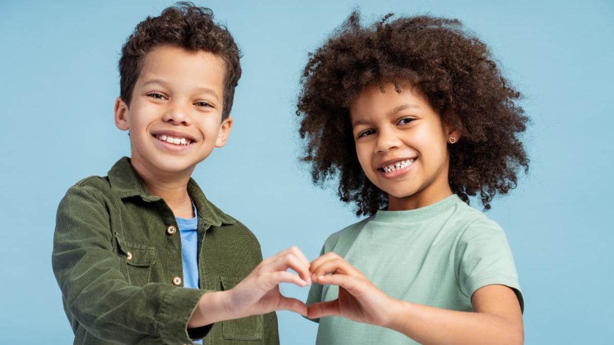 Two elementary age children stand together holding their hands in a heart shape.
