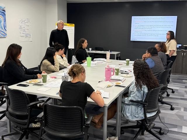 9 training participants listen to 2 presenters in a conference room