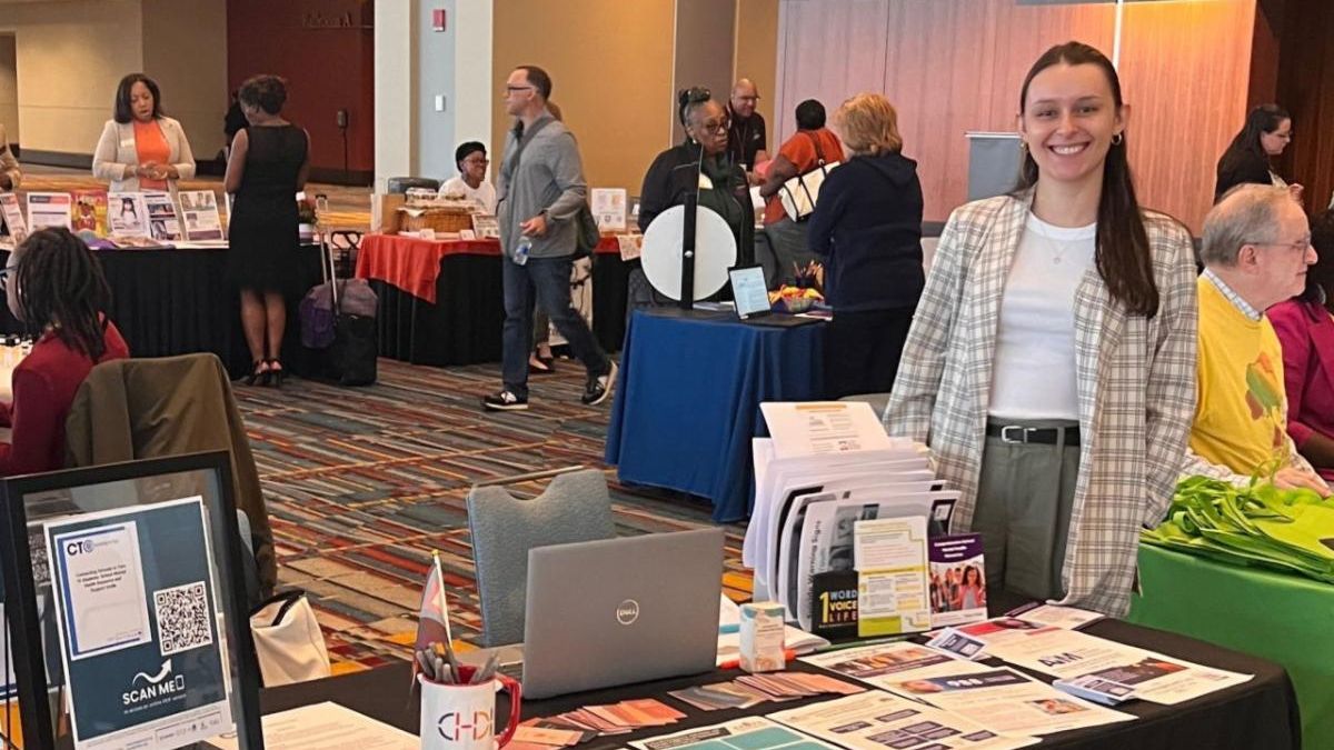 CHDI's Sarah White standing behind an information table at the SERC Conference