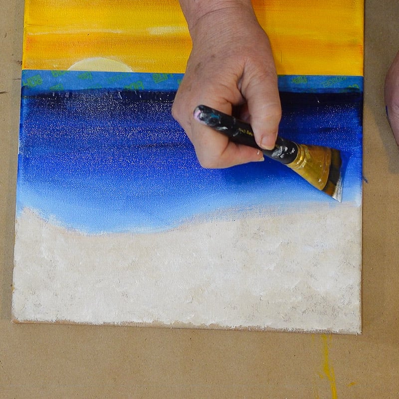 Close up of a hand painting a sunset over the ocean on canvas