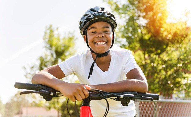 A young boy with a helmet on, leaning on his bike handlebars